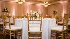 Gold chiavari chairs with white cushions at round tables in a warmly lit wedding reception ballroom